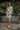 Full front view of model wearing the Look On The Bright Side Dress that has a pink, green, blue, yellow and cream flower pattern, a mini-length hem, an elastic waist with a tie, a surplice neck, and long balloon sleeves.