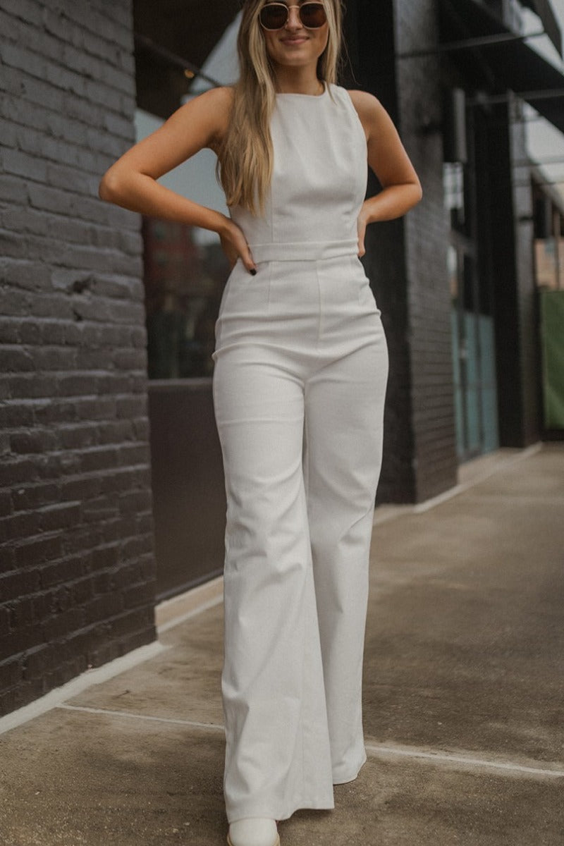 Front view of model wearing the Ready To Go Denim Jumpsuit that has white denim fabric, a round neckline, a thick waistband, a back zipper and hook closure, a sleeveless body, and wide flared legs