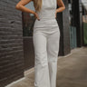 Front view of model wearing the Ready To Go Denim Jumpsuit that has white denim fabric, a round neckline, a thick waistband, a back zipper and hook closure, a sleeveless body, and wide flared legs