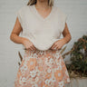 Front view of model wearing the Favorite Flowers Skirt that has light brown, rust and cream fabric with a floral pattern, a mini-length hem, a smocked waistband, and a lining