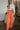 Full body front view of model wearing the Pop Of Color Pants that feature orange fabric, side pockets, a front zipper with a hook closure, and wide legs with pleated details.