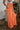 Side view of model wearing the Pop Of Color Pants that feature orange fabric, side pockets, a front zipper with a hook closure, and wide legs with pleated details.