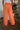 Back view of model wearing the Pop Of Color Pants that feature orange fabric, side pockets, a front zipper with a hook closure, and wide legs with pleated details.