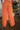 Back view of model wearing the Pop Of Color Pants that feature orange fabric, side pockets, a front zipper with a hook closure, and wide legs with pleated details.