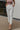 Front view of model wearing the Working For The Weekend Pants that have off white fabric, two front pockets, two back pockets, a front zipper and clasp closure, an elastic-back waist with belt loops, and flared legs.