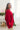 Side view of model wearing the Bristol Oversized Satin Top in Red that has red satin fabric, a button-up front with a collared neckline, one chest pocket, long sleeves with buttoned cuffs, and an oversized fit