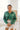 Front view of model wearing the Fancy Me Satin Top in Green which features emerald green satin fabric, a button-up front with a collared neckline, one chest pocket, and long sleeves with buttoned cuffs. Blouse is tucked. 