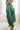 Side view of model wearing the Fancy Me Satin Top in Green which features emerald green satin fabric, a button-up front with a collared neckline, one chest pocket, and long sleeves with buttoned cuffs.