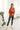 Full body view of model wearing the Fancy Me Satin Top in Rust which features rust satin fabric, a button-up front with a collared neckline, one chest pocket, and long raglan sleeves with buttoned cuffs.