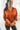 Front view of model wearing the Fancy Me Satin Top in Rust which features rust satin fabric, a button-up front with a collared neckline, one chest pocket, and long raglan sleeves with buttoned cuffs.