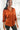 Front view of model wearing the Fancy Me Satin Top in Rust which features rust satin fabric, a button-up front with a collared neckline, one chest pocket, and long raglan sleeves with buttoned cuffs.