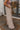 Side view of model wearing the Keep It Classic Pants that have khaki colored fabric, two front pockets, a front zipper and hook closure, belt loops, and wide legs with pleated details.