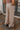 Back view of model wearing the Keep It Classic Pants that have khaki colored fabric, two front pockets, a front zipper and hook closure, belt loops, and wide legs with pleated details.
