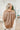 Back view of model wearing the Bristol Oversized Satin Top in Mocha that has light brown satin fabric, a button-up front with a collar, one chest pocket, long sleeves with buttoned cuffs, and an oversized fit. 