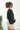 Side view of model wearing the Checked Out Cropped Satin Top that has black satin fabric with a monochromatic checker print, a surplice neck, a cropped waist, and long batwing sleeves.