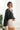 Side view of model wearing the Checked Out Cropped Satin Top that has black satin fabric with a monochromatic checker print, a surplice neck, a cropped waist, and long batwing sleeves.