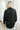 Back view of the Fancy Me Satin Top in Black which features black satin fabric, a button-up front with a collared neckline, one chest pocket, and long raglan sleeves with buttoned cuffs.