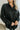 Close up view of the Fancy Me Satin Top in Black which features black satin fabric, a button-up front with a collared neckline, one chest pocket, and long raglan sleeves with buttoned cuffs.