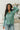 Front view of model wearing the Spot On Satin Top in Jade that has light teal satin fabric with a monochromatic spot print, a button-up front with a collar and lapels, and long sleeves with buttoned cuffs