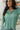 Front view of model wearing the Spot On Satin Top in Jade that has light teal satin fabric with a monochromatic spot print, a button-up front with a collar and lapels, and long sleeves with buttoned cuffs