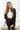 Front view of model wearing the Aria Oversized Satin Top in Black that has black satin fabric, a button-up front with a collar, one pocket and long sleeves. Worn unbuttoned over white top