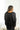 Back view of model wearing the Aria Oversized Satin Top in Black that has black satin fabric, a button-up front with a collar, one pocket and long sleeves.