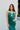 Close-up front view of model wearing the Life Of The Party Maxi Dress which has an emerald green satin material, a deep open neckline, thin adjustable straps, a side drape detail with a slit, an open back, and a back zipper closure.