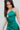 Close-up side view of model wearing the Life Of The Party Maxi Dress which has an emerald green satin material, a deep open neckline, thin adjustable straps, a side drape detail with a slit, an open back, and a back zipper closure.