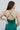 Close-up back view of model wearing the Life Of The Party Maxi Dress which has an emerald green satin material, a deep open neckline, thin adjustable straps, a side drape detail with a slit, an open back, and a back zipper closure.
