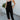 Full body front view of model wearing the Next Adventure Jumpsuit in Black, which features a black linen material, a square neck, a sleeveless design with tie straps, two front and back pockets, and elastic ankles. Worn over white tank.