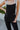 Close-up front view of model wearing the Next Adventure Jumpsuit in Black, which features a black linen material, a square neck, a sleeveless design with tie straps, two front and back pockets, and elastic ankles. Worn over white tank.