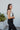 Close-up side view of model wearing the Next Adventure Jumpsuit in Black, which features a black linen material, a square neck, a sleeveless design with tie straps, two front and back pockets, and elastic ankles. Worn over white tank.