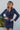 Front view of model wearing the First Impressions Dress, which has a navy colored material, a collar neck, a surplice neckline, a long cuffed sleeve, a side draping detail, and a mini length.