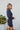 Side view of model wearing the First Impressions Dress, which has a navy colored material, a collar neck, a surplice neckline, a long cuffed sleeve, a side draping detail, and a mini length.