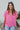 Front view of model wearing the First Class Top, which has a bubble gum pink material, a collar neckline, a button-up front, a front pocket, short cuffed sleeves, and a flowy fit