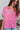 Front view of model wearing the First Class Top, which has a bubble gum pink material, a collar neckline, a button-up front, a front pocket, short cuffed sleeves, and a flowy fit