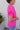 Side view of model wearing the Irreplaceable Top In Pink, which features a hot pink material, a round neckline with a ruffle detail, a cut-out at the chest with adjustable ties, a short smocked sleeve, and a flowy fit