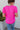 Back view of model wearing the Irreplaceable Top In Pink, which features a hot pink material, a round neckline with a ruffle detail, a cut-out at the chest with adjustable ties, a short smocked sleeve, and a flowy fit