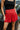 Close-up front view of model wearing the Game On Shorts, which feature a red shimmer material, a smocked waist, a high-rise fit, a ruffle top hem, and a flowy fit.