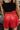 Back view of model wearing the Game On Shorts, which feature a red shimmer material, a smocked waist, a high-rise fit, a ruffle top hem, and a flowy fit.