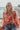 Frontal view of the All Class Top that features a salmon colored chiffon material, a floral print, a collar neck, a long cuffed sleeve, and a back elastic hemline.