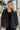Frontal view of the Serious Chill Denim Jacket that features an ash black denim material, a collar neck, a button-up front, long cuffed sleeves, two front pockets, a frayed bottom hem, and an oversized fit.