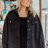 Frontal view of the Serious Chill Denim Jacket that features an ash black denim material, a collar neck, a button-up front, long cuffed sleeves, two front pockets, a frayed bottom hem, and an oversized fit.