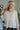 Frontal view of the Easy Breezy Top that features a cream colored knit material, an open knit design, a V neckline, a long cuffed sleeve, side slits, and a high-low design.