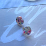 The Lover Earring is an acrylic, stud style earring, featuring a heart shaped body with a multi-colored design.