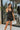 Frontal view of the City Walk Dress that features a black silky material, a cowl neckline, a sleeveless design with thin adjustable straps, a tie at the waist, a draped design, a back zipper closure, and a mini length.