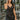 Frontal view of the City Walk Dress that features a black silky material, a cowl neckline, a sleeveless design with thin adjustable straps, a tie at the waist, a draped design, a back zipper closure, and a mini length.
