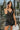 Frontal view of the City Walk Dress that features a black silky material, a cowl neckline, a sleeveless design with thin adjustable straps, a tie at the waist, a draped design, a back zipper closure, and a mini length.