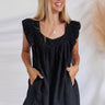 Frontal view of the End Game Romper that features a black cotton material, a rounded v neckline, a sleeveless design with tick straps, ruffle details at the straps, side pockets, a shorts bottom, a tie back, and a flowy fit.