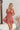 Frontal view of the Mystic Meadows Dress that features a light clay material, a scoop neckline with a tie detail, a half sleeve, a ruched elastic waist, a two-tiered bottom with a ruffle hem, a squared back, and a mini length.
